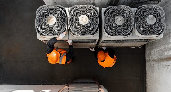melhores empresas de climatização - Dois operários estão a verificar algumas unidades de ar condicionado no telhado de um edifício.